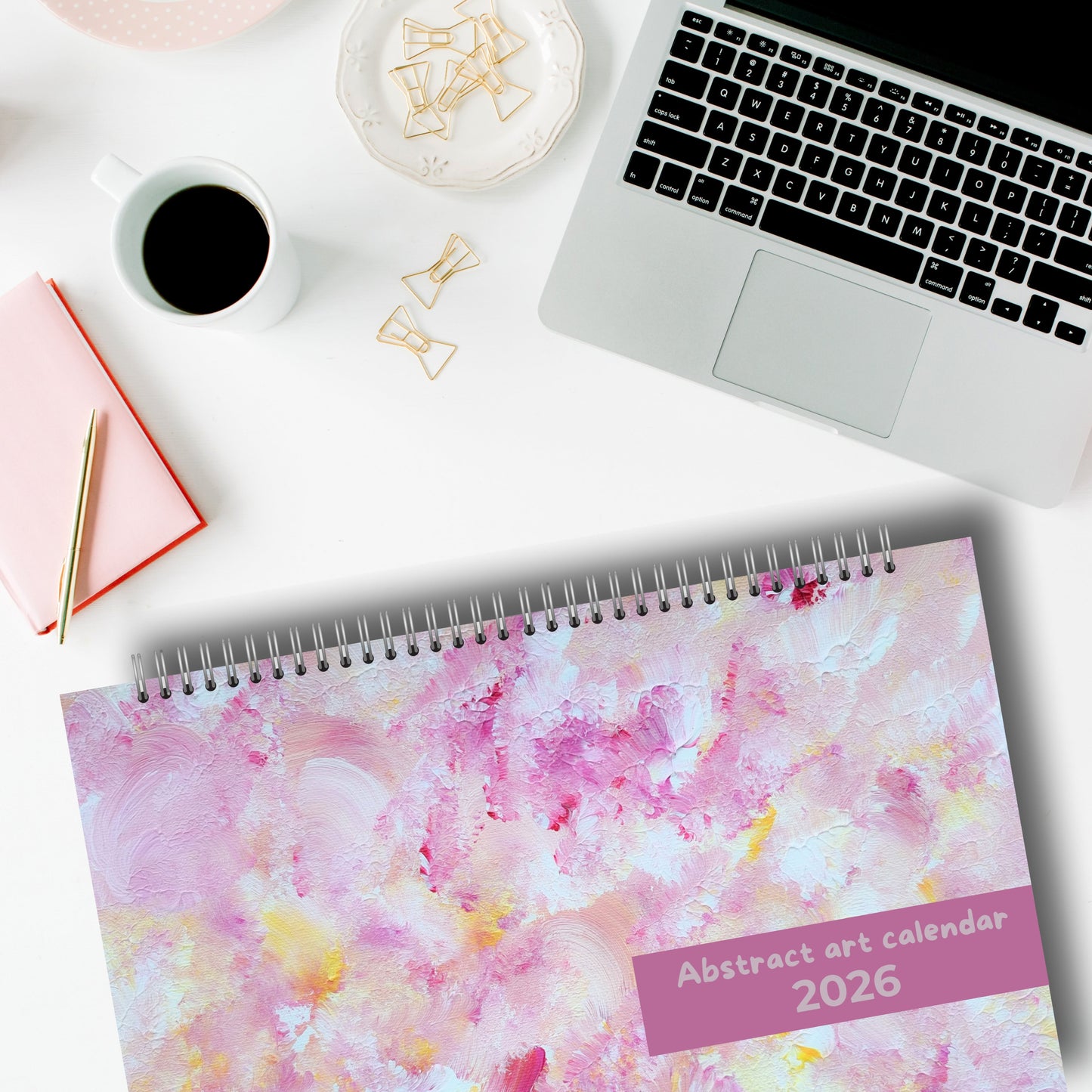 horizontal pink art calendar laying on a desk with a laptop in a modern and white home office