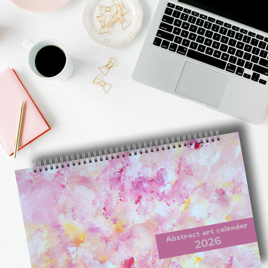 horizontal pink art calendar laying on a desk with a laptop in a modern and white home office