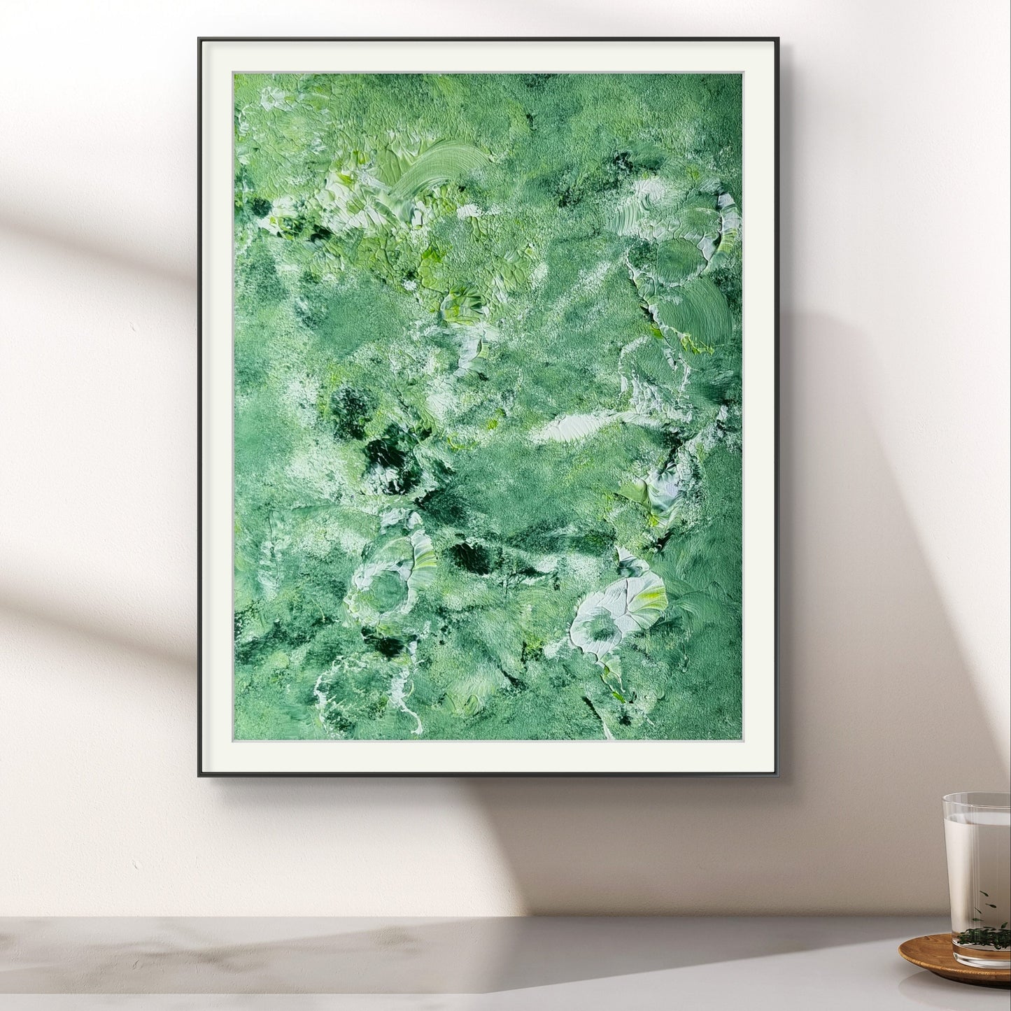 Green and white abstract painting in a black frame on a white wall over a marble table created by up-and-coming artist Jeanette Haga as decor for modern homes