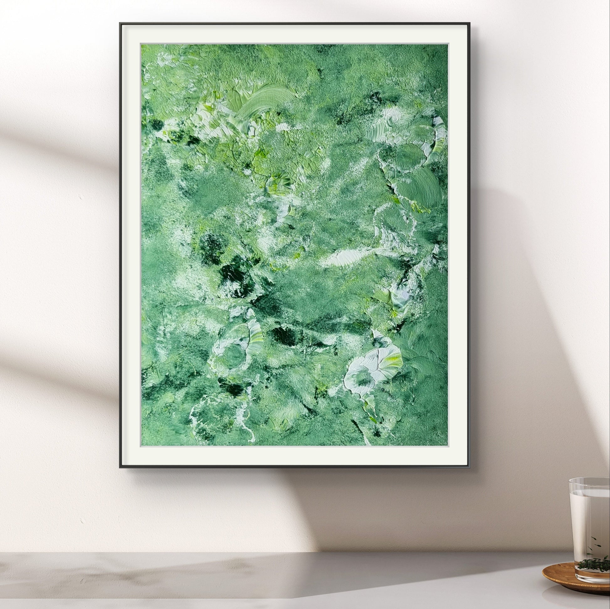 Green and white abstract painting in a black frame on a white wall over a marble table created by up-and-coming artist Jeanette Haga as decor for modern homes