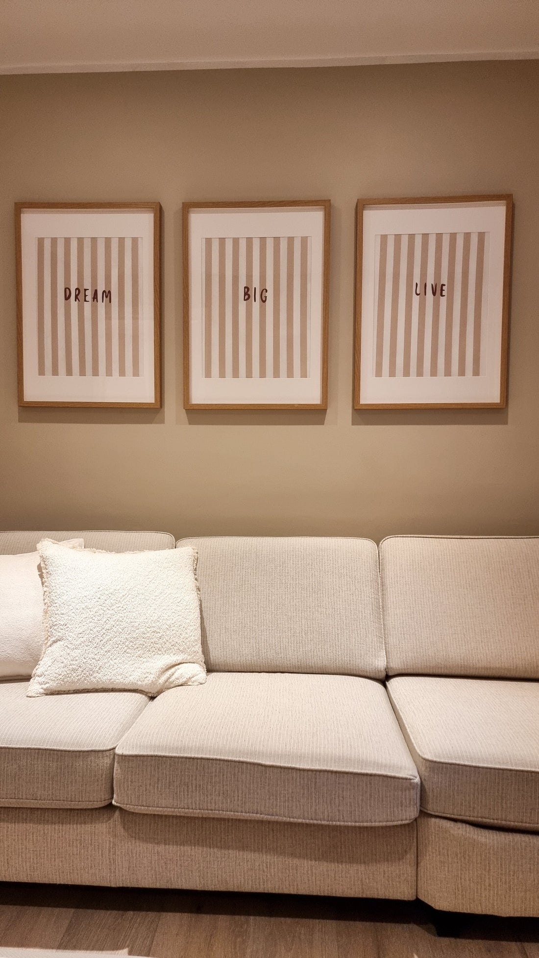 Three wood-framed striped prints reading Dream, Big, and Live above a cream sofa.