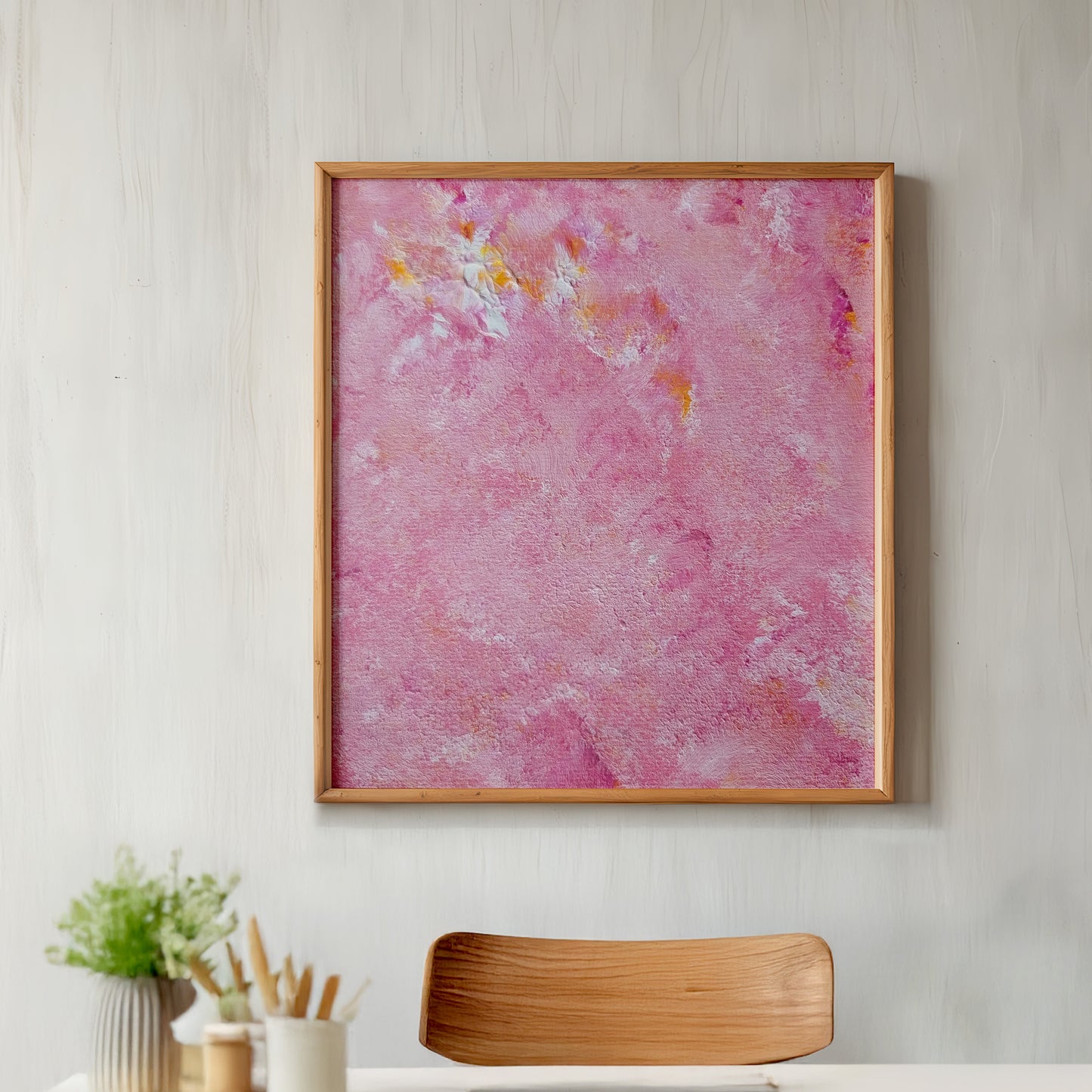 Framed abstract pink artwork on a wall above a desk with a chair.