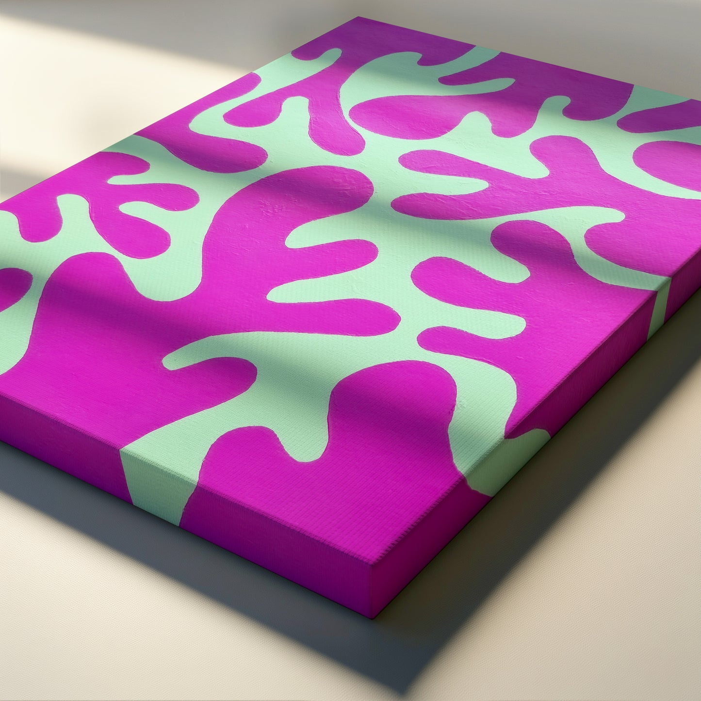 A rectangular canvas print featuring a bold abstract pattern of bright magenta and mint green organic shapes, shown at an angle on a light beige surface with soft shadows.