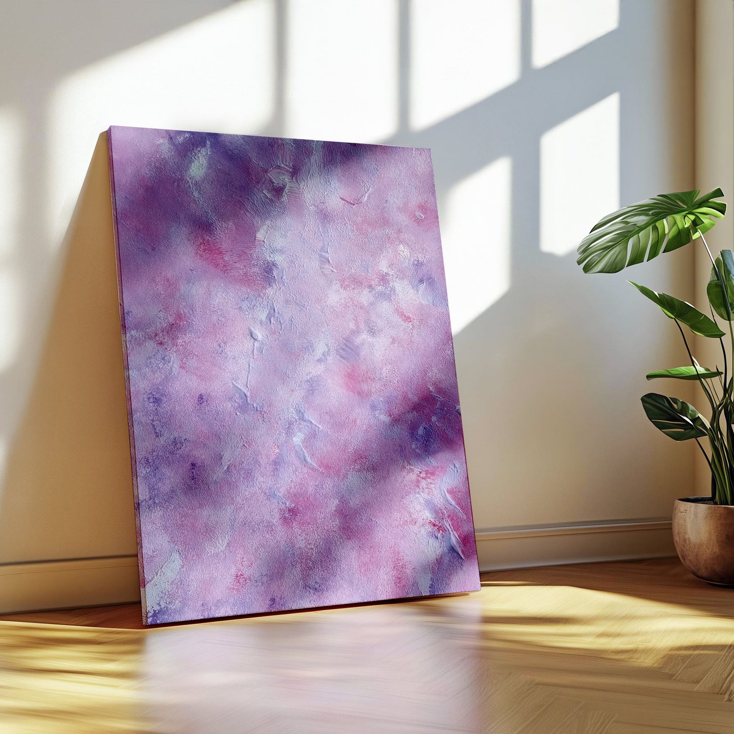 A vertical canvas print with a purple and pink watercolor abstract pattern, leaning against a beige wall on a wooden floor next to a potted green plant.