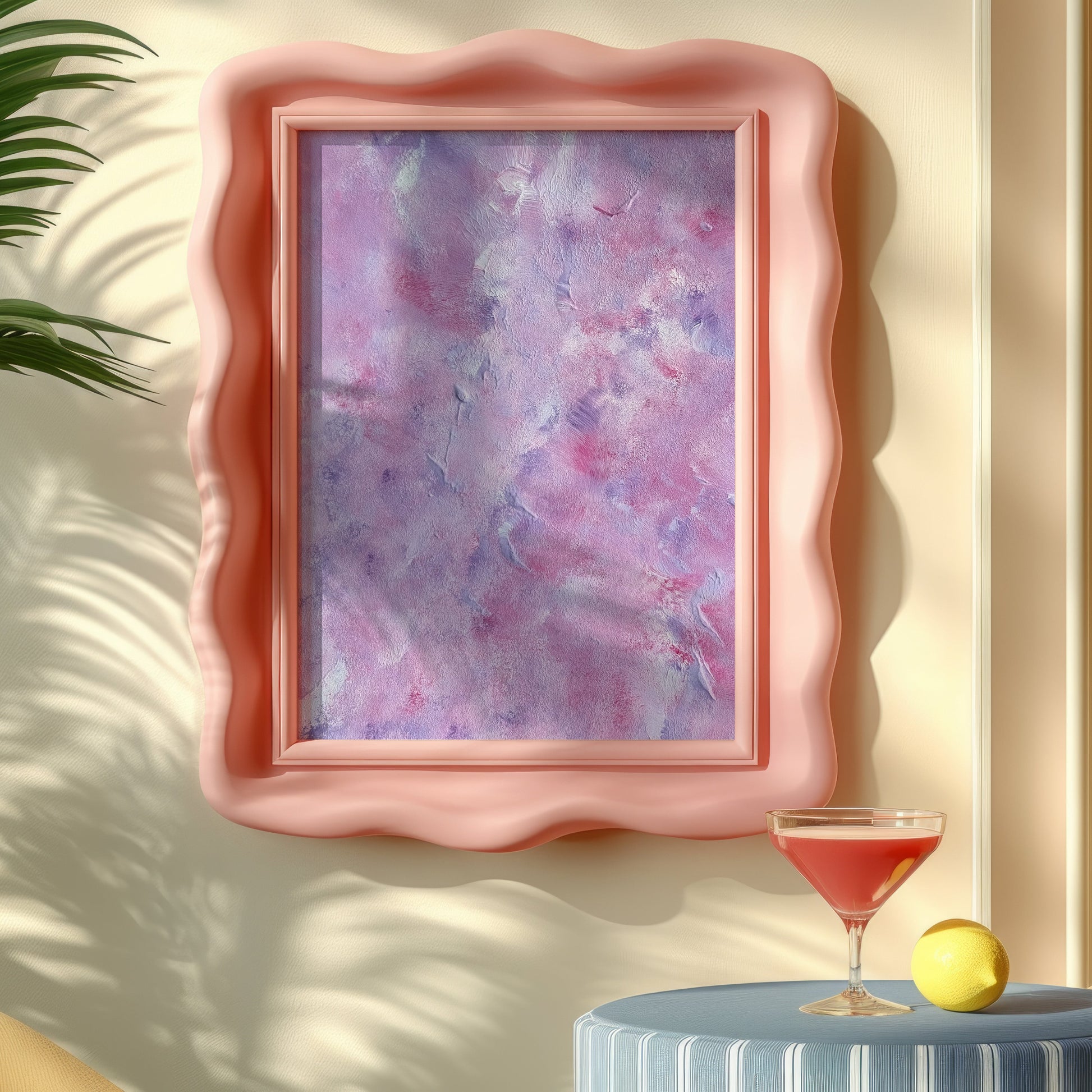 A wavy pink picture frame holding an abstract purple and pink painting, styled on a beige wall with a cocktail glass, lemon, and plant leaves in a sunlit interior.