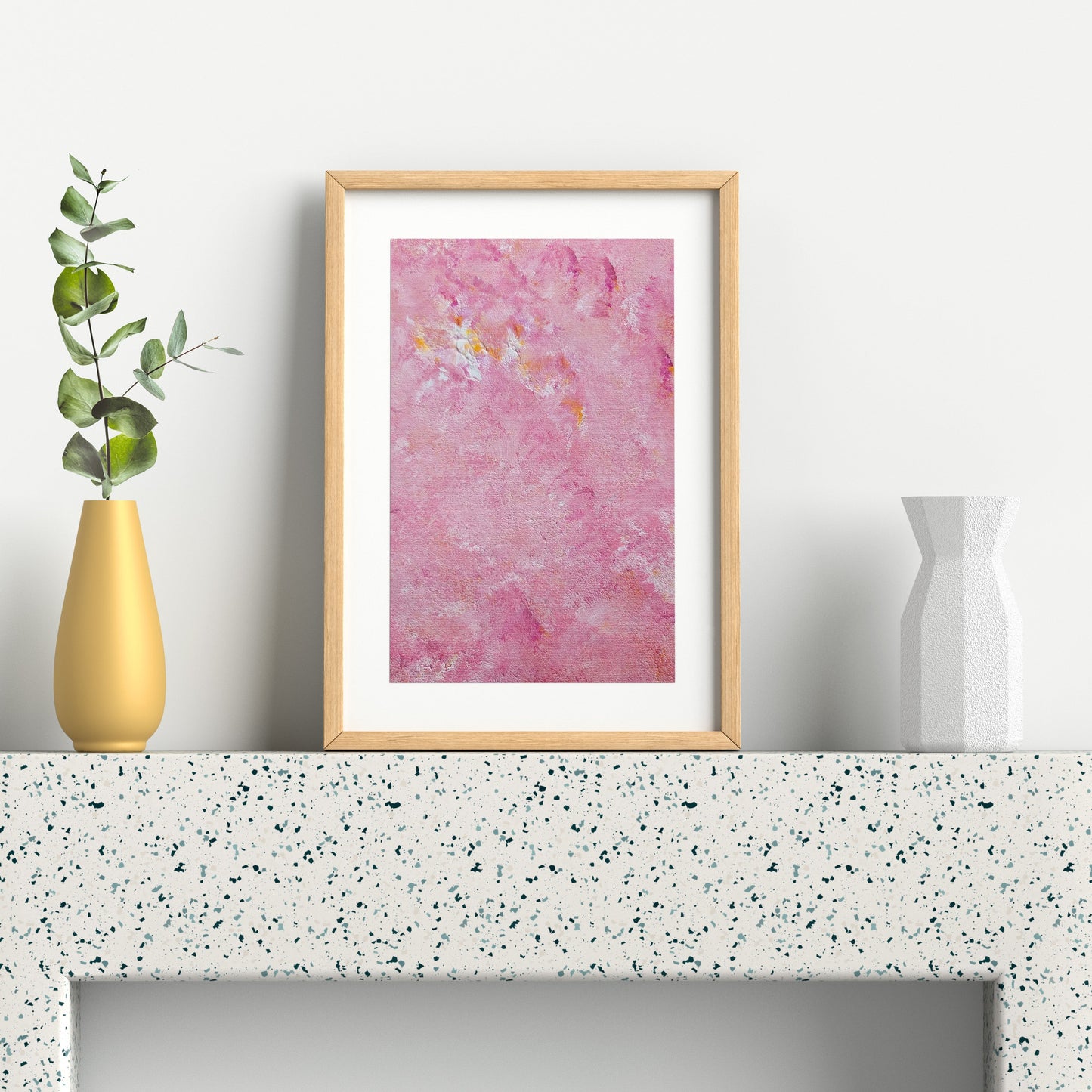 Framed pink watercolor painting on a white shelf with a yellow vase and green leaves.