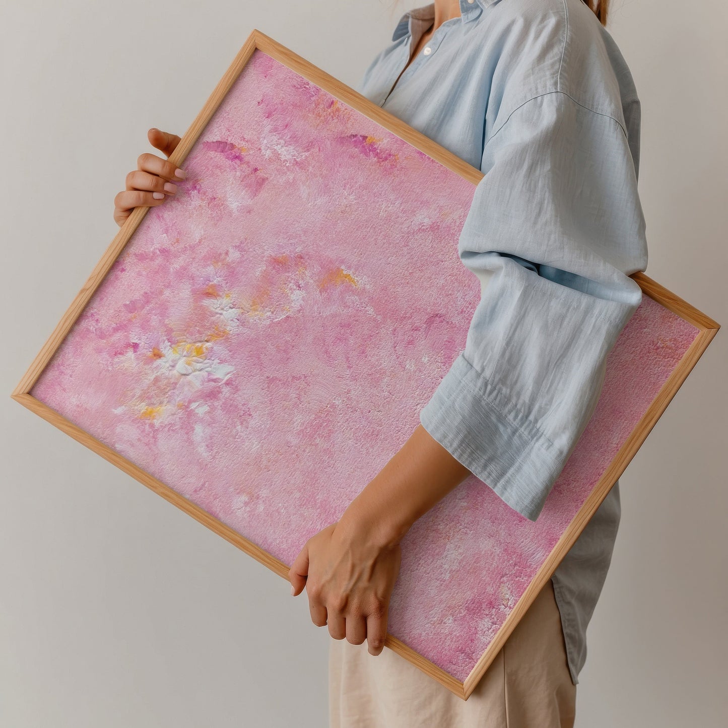 Person holding a pink framed artwork against a plain background