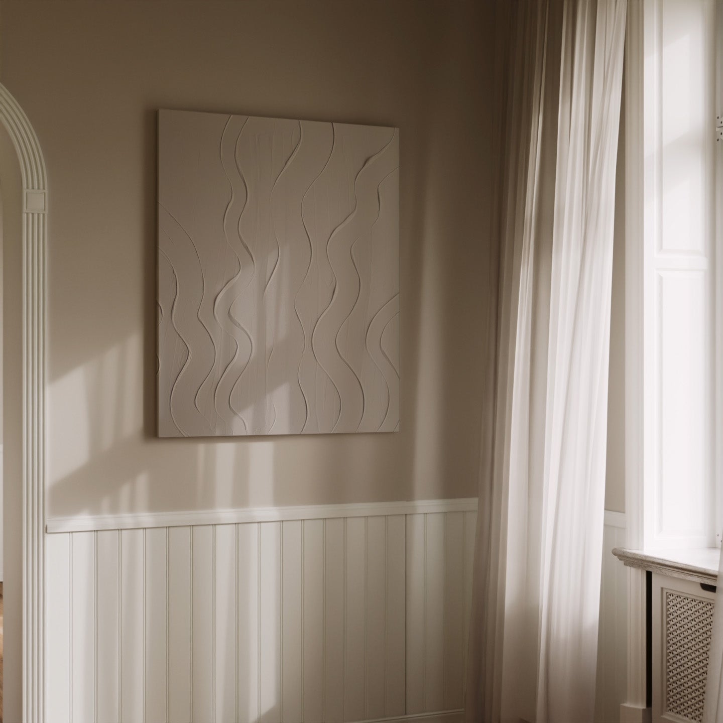 A square wall art piece with a textured, raised wavy pattern in a warm off-white tone, displayed on a beige wall in a softly lit room with white wainscoting, sheer curtains, and a window.