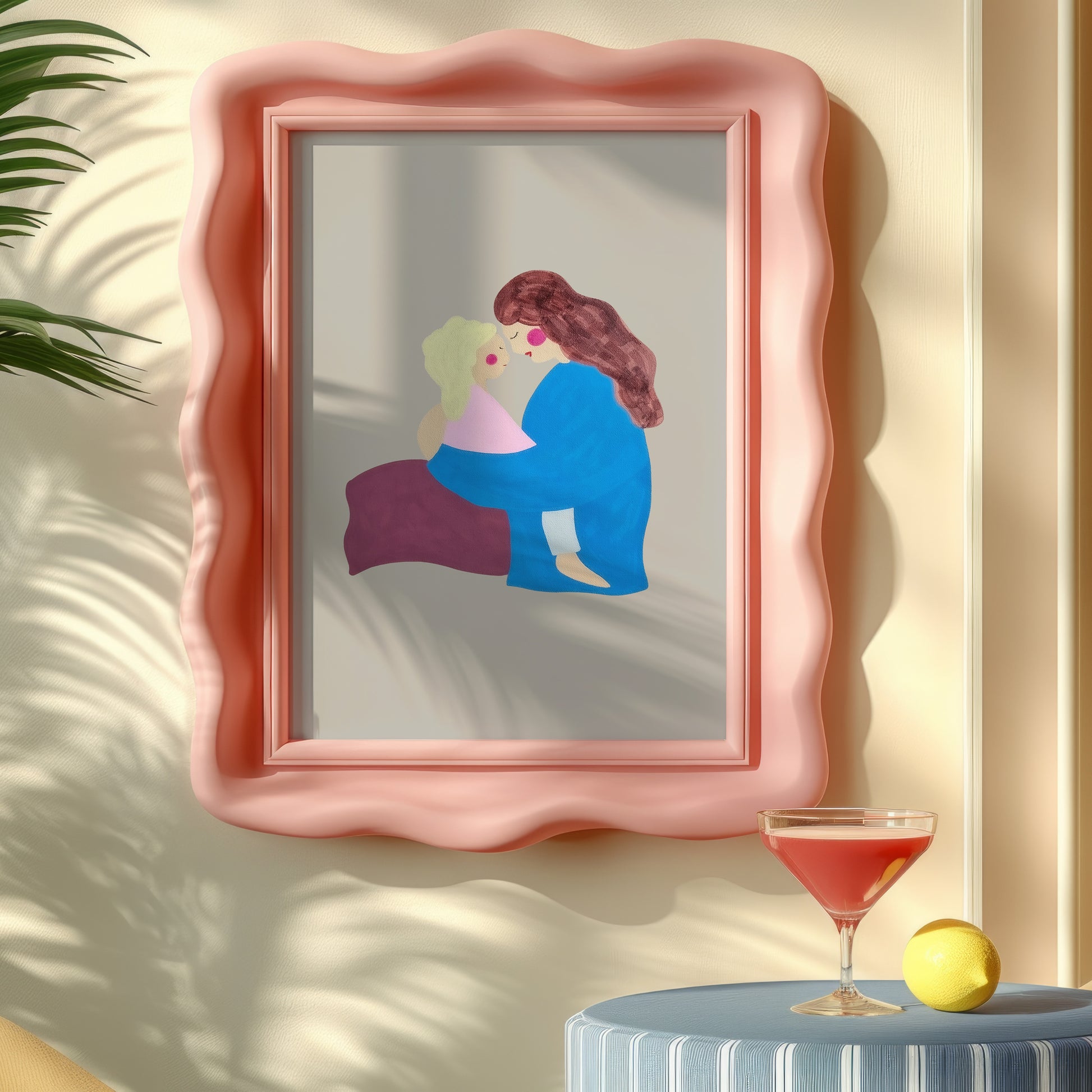 A framed art print featuring a stylized illustration of two embracing figures, displayed on a beige wall in a styled interior setting with a cocktail glass and lemon nearby.
