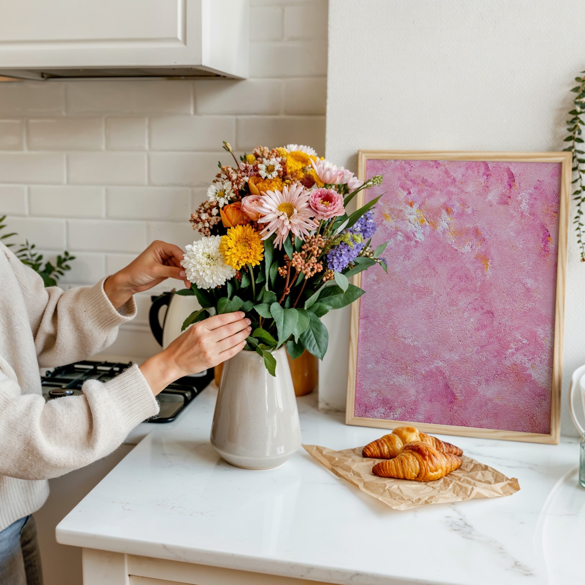 Person arranging flowers in a kitchen with a pink abstract painting on the wall.