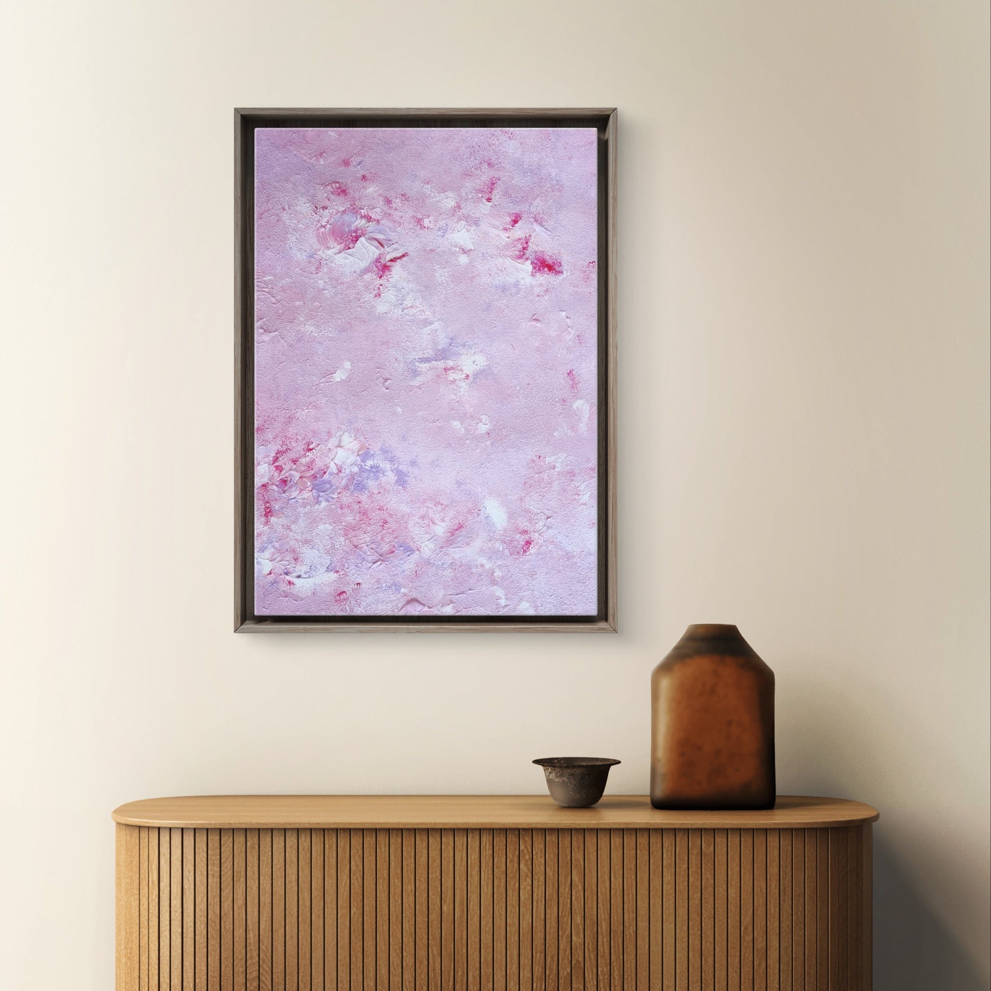 Original one of a kind colorful abstract acrylic art piece in pink, lilac and red, hanging vertically against a beige wall as decor over modern light wood furniture