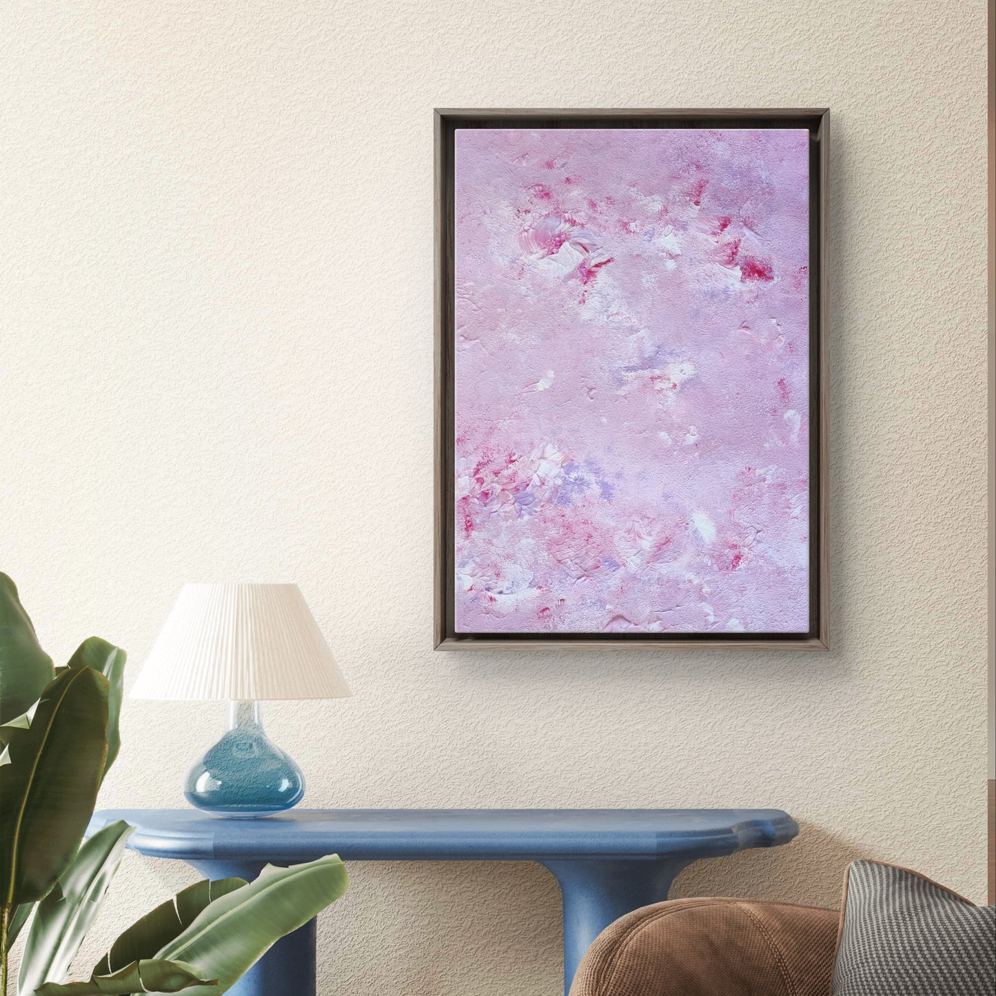 Original abstract acrylic art piece in pink, lilac and red, hanging vertically against a white brick wall in a living room with earthly tones and green plants