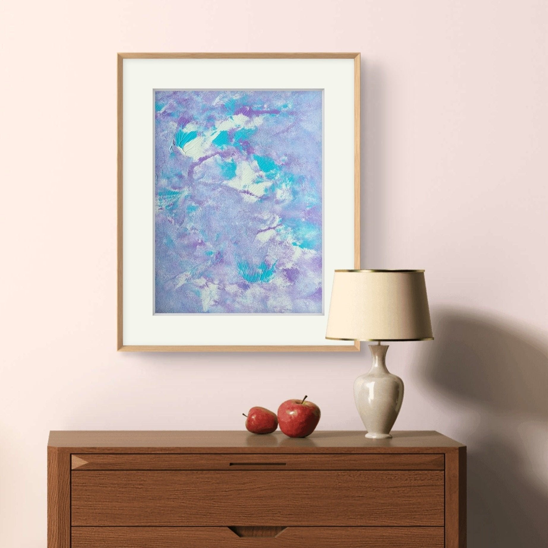 Original one of a kind colorful abstract acrylic art piece in pastel purple, blue and white, hanging vertically against a pink wall as decor over a brown wooden dresser with a decor lamp on top