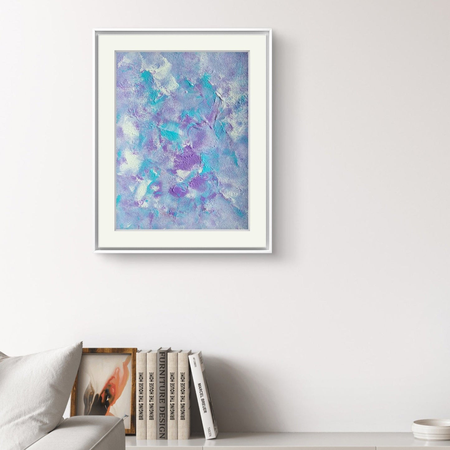 Original one of a kind colorful abstract acrylic art piece in pastel purple, blue and white, hanging vertically against a white wall as decor in a modern living room with light furniture