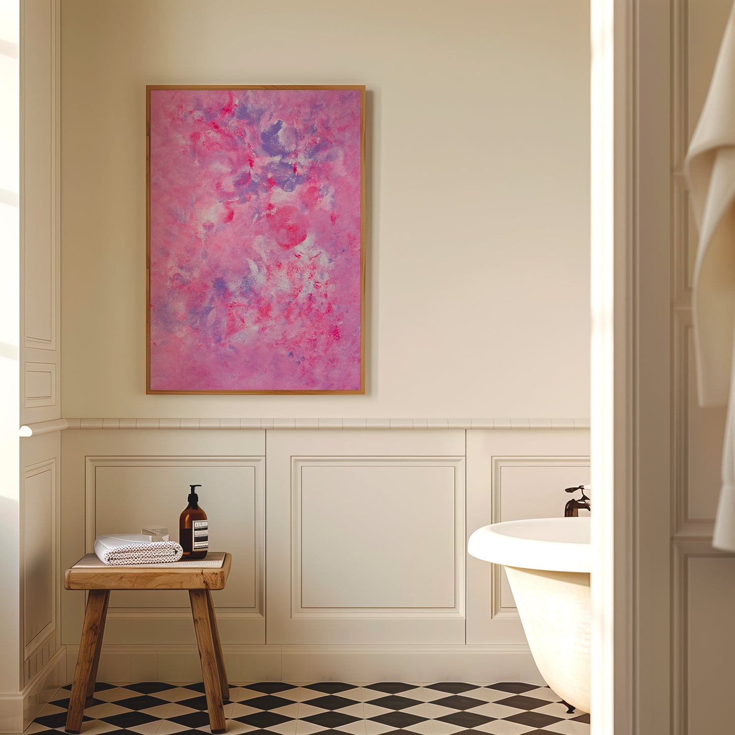 A framed abstract painting with vibrant pink, purple, and blue brushstrokes hangs on a cream-colored bathroom wall above wainscoting, next to a small wooden stool and a white bathtub.