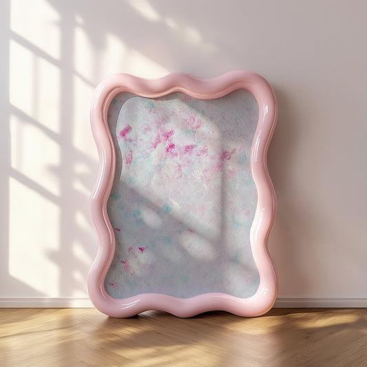 A wavy-edged pink mirror leaning against a light beige wall on a wooden floor, with soft window shadow patterns cast across the reflective surface.