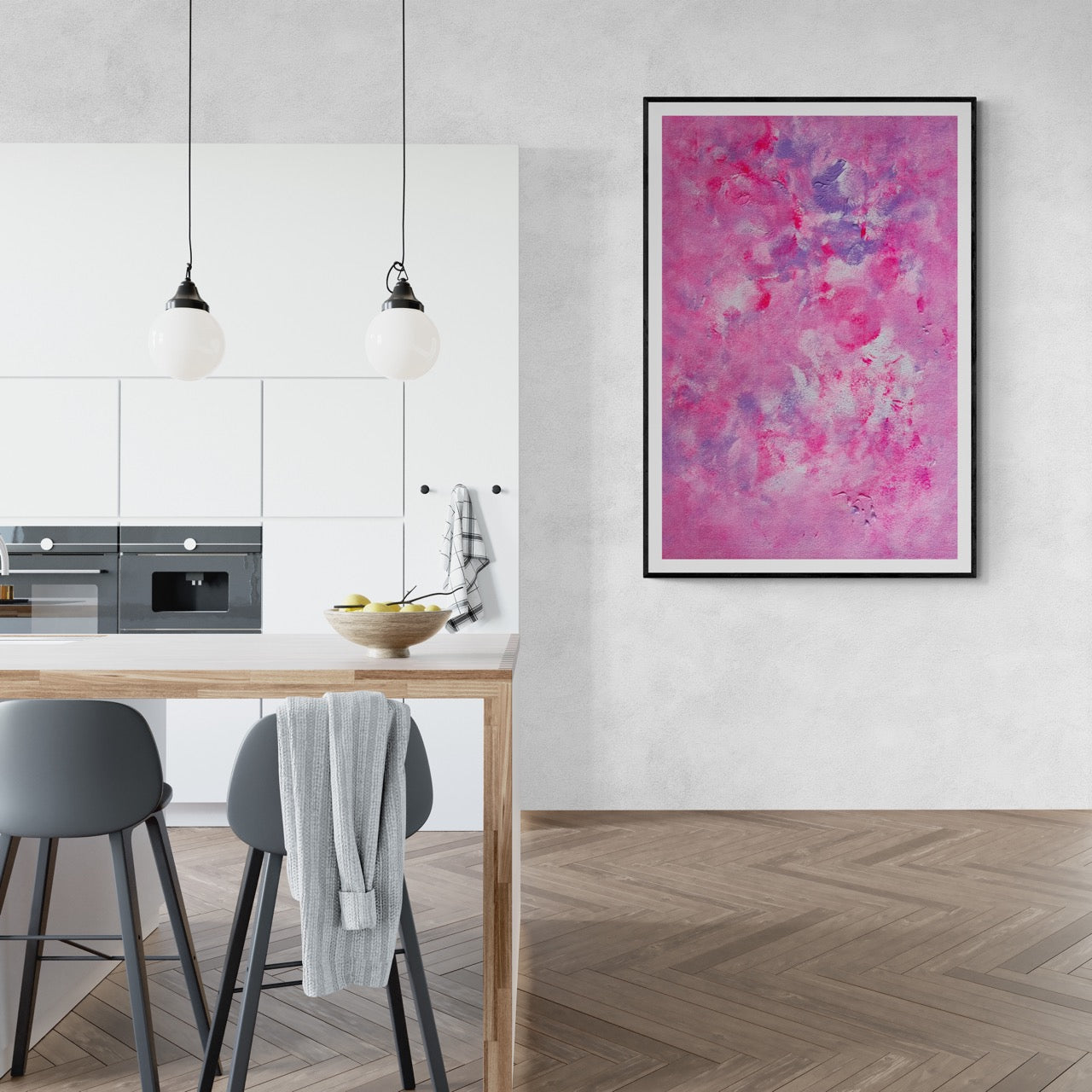 Pink, purple and white abstract art poster with a black frame hanging vertically on a white wall next to a minimalistic white kitchen. The floor is wood and herringbone pattern and there is a dining room table in front