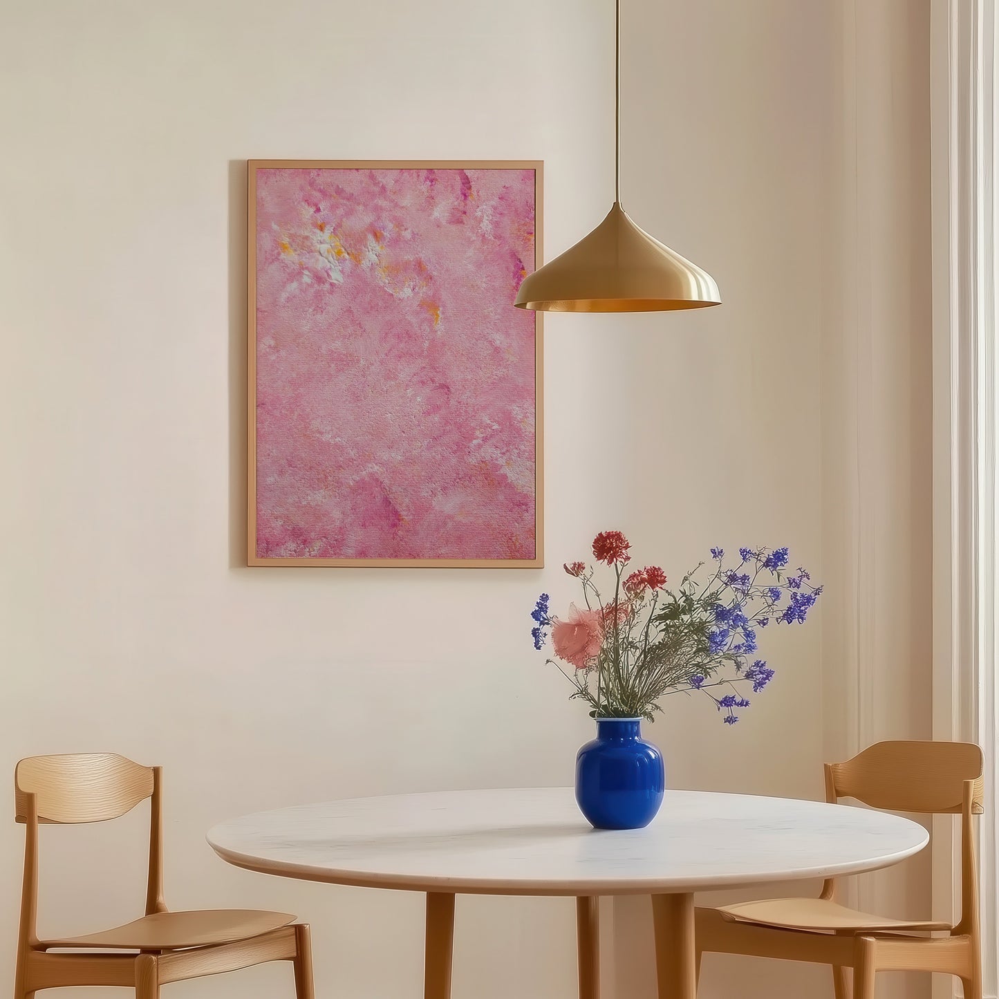 Dining room with a round table, chairs, and a vase of flowers on a white wall with a pink floral painting.