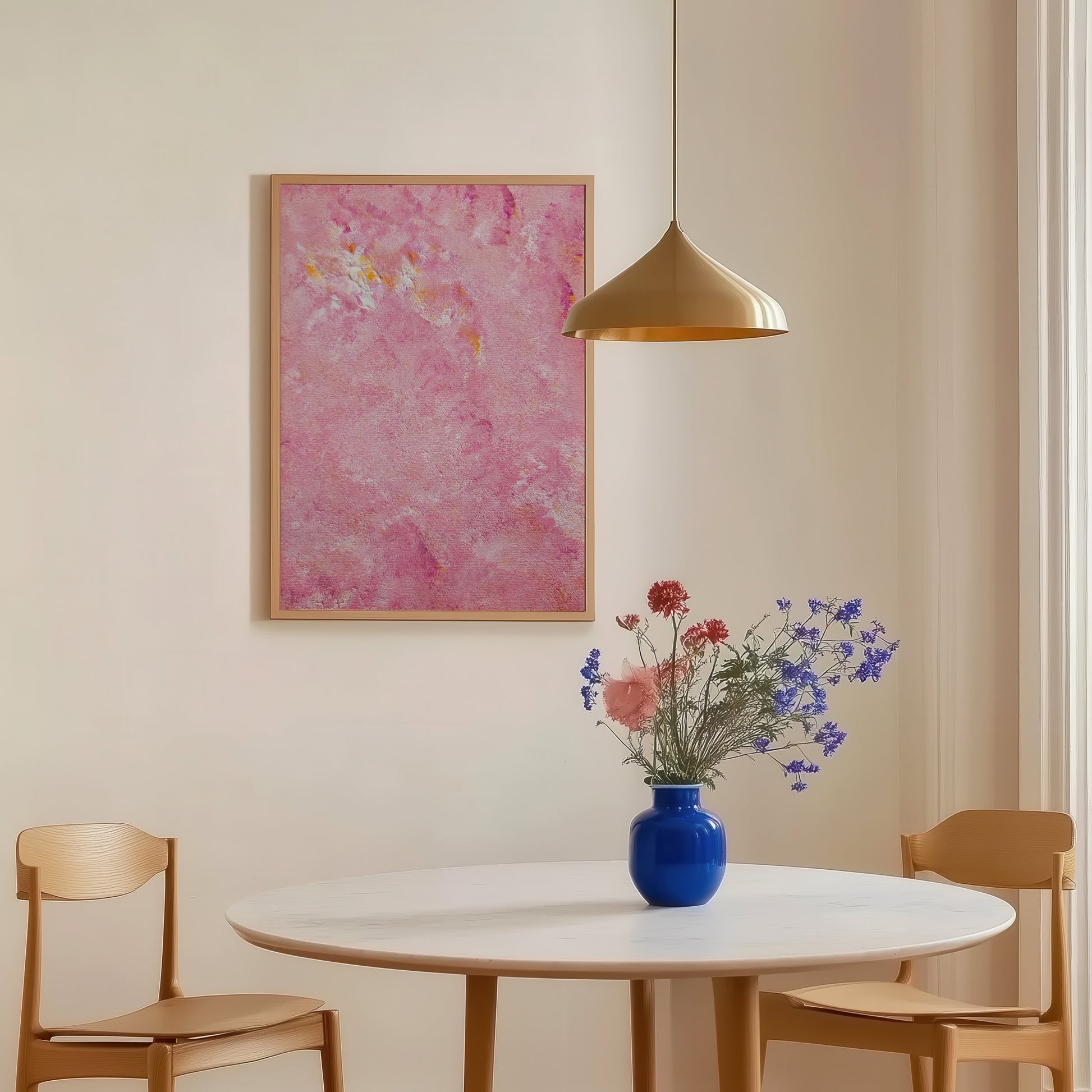 Dining room with a round table, chairs, and a vase of flowers on a white wall with a pink floral painting.